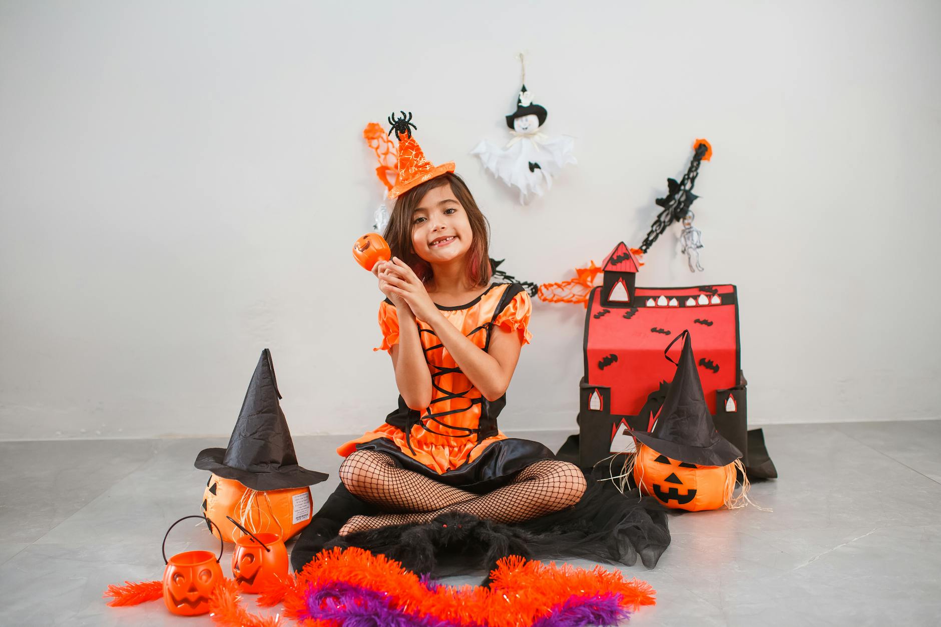 Dziewczynka w stroju czarownicy wśród halloweenowych dekoracji